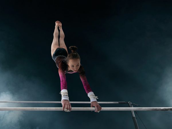 Female gymnast doing a complicated trick on gymnastic horizontal bar.