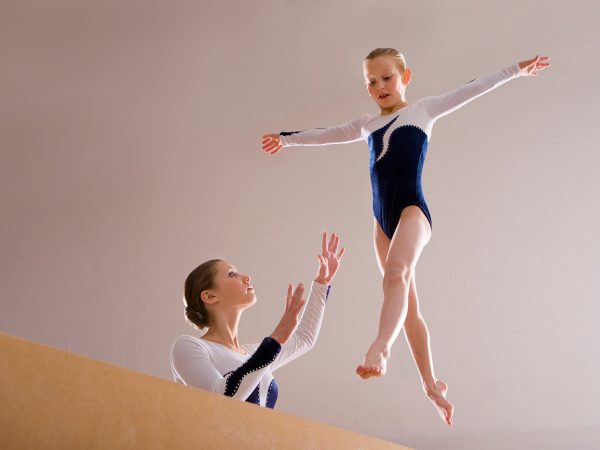 Low angle view of a gymnastics instructor teaching girl on a balance beam.